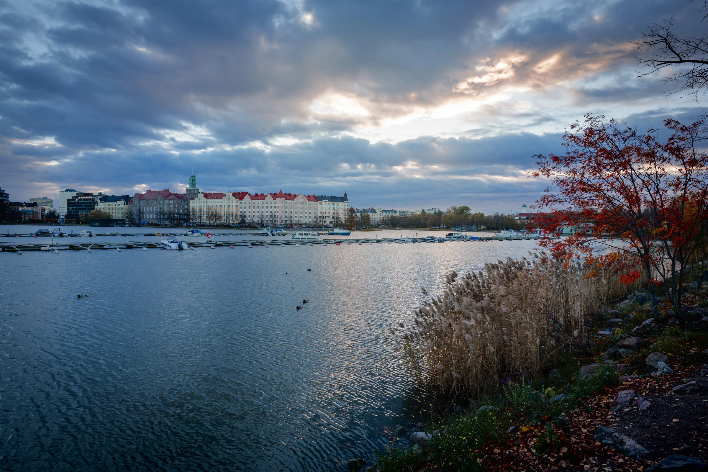 A lake in the city during autumn, with sunlight breaking through some dramatic clouds.